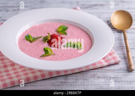 Süße kalte Erdbeersuppe mit grünem Minzblatt in einer weißen Schüssel auf einem Holztisch, Nahaufnahme Stockfoto