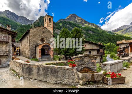 Alte Pfarrkirche und Häuser als Berge unter blauem Himmel im kleinen alpinen Dorf Chianale in Piemont, Italien. Stockfoto