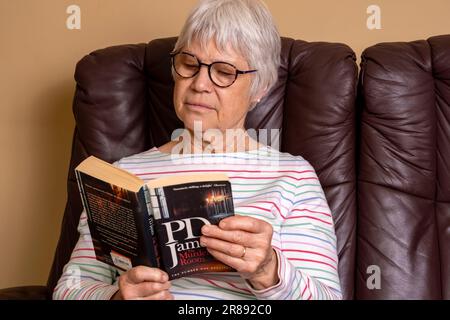 Eine Frau, die sich zu Hause entspannt und einen PD James Roman liest Stockfoto