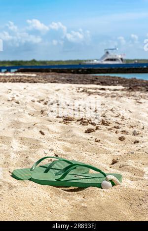 Nahaufnahme von einem Paar grünen Flip-Flops auf dem Sand eines karibischen Strands bei Tageslicht unter direkter Sonneneinstrahlung im Sommer Stockfoto