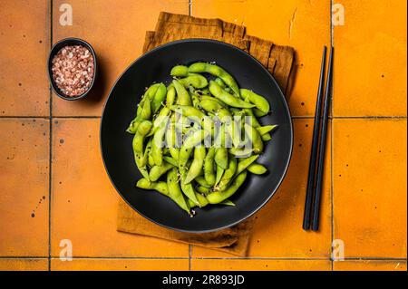 Gekochte Edamam-Sojabohnen mit Meersalz und Sesamsamen. Orangefarbener Hintergrund. Draufsicht. Stockfoto