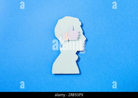 Ein Papierausschnitt aus dem Kopf eines Mannes mit einem ähnlichen Symbol auf blauem Hintergrund Stockfoto