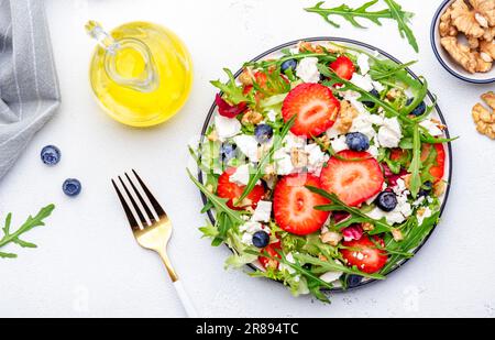 Erdbeersalat mit Rucola, Kopfsalat, Blaubeeren, Fetakäse und Walnüssen, weißer Tisch. Frisches, nützliches Gericht für gesunde Ernährung Stockfoto