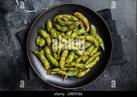 Gebratene grüne Edamame-Sojabohnen mit Meersalz und Sesamsamen auf einem Teller. Schwarzer Hintergrund. Draufsicht. Stockfoto