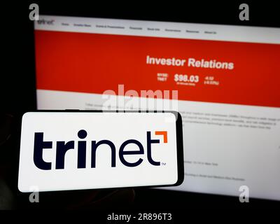 Person, die ein Mobiltelefon mit dem Logo des amerikanischen Outsourcing-Unternehmens TriNet Group Inc. Auf dem Bildschirm vor der Webseite hält. Konzentrieren Sie sich auf das Display des Telefons. Stockfoto