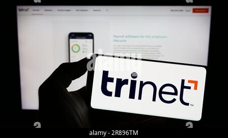 Person, die ein Mobiltelefon mit dem Logo des US-Outsourcing-Unternehmens TriNet Group Inc. Auf dem Bildschirm vor der Unternehmenswebseite hält. Konzentrieren Sie sich auf das Display des Telefons. Stockfoto