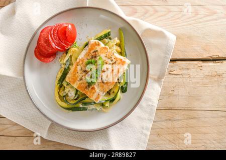 Wildlachsfilet mit Petersilie, Zucchini-Gemüse und Tomaten auf einem leichten Teller und einem rustikalen Holztisch, gesunde kohlenhydratarme Diät, High a Stockfoto