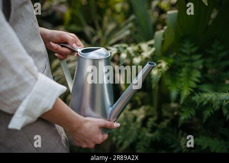 Eine Frau, die eine Gießkanne hält, Pflanzen in einem Gewächshaus gießt. Stockfoto