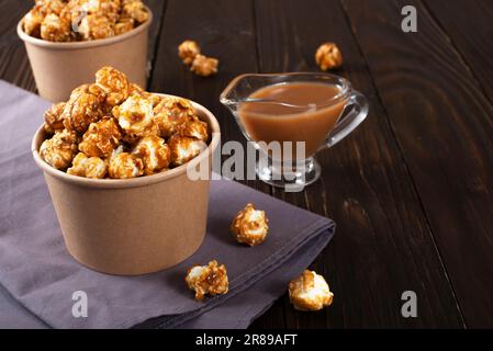 Karamellisiertes Popcorn in Papiereimer auf Holztisch Stockfoto