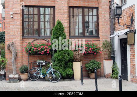 Der Hinterhof eines alten roten Backsteinhauses in der polnischen Stadt Danzig mit zwei großen Fenstern, einer Hintertür und Blumenbeeten Stockfoto