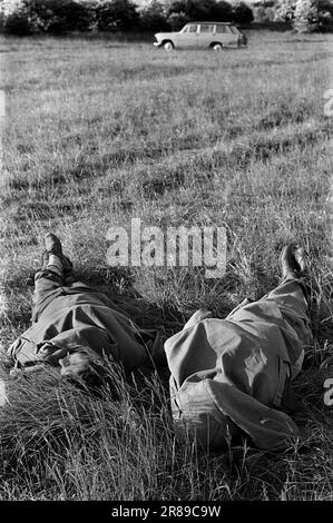 Betrunken ausschlafen, einen Kater. Ein Tag bei den Rennen, zwei Männer bedecken ihre Gesichter in ihren Mänteln, sie schlafen am Ende des Derby, einem jährlichen Pferderennveranstaltungsfestival. Epsom Downs, Surrey, England, ca. 1970 1970er. Juni, Großbritannien. Stockfoto