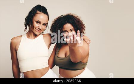 Zwei junge Frauen in Sportbekleidung führen mit Energie und Vitalität einen erlebnisreichen Tanz und eine sportliche Übung in einem Studio durch. Fröhliche Sportlerinnen feiern Stockfoto