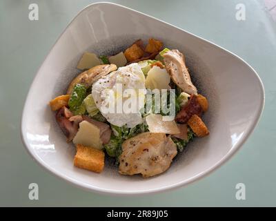 Caesar-Salat mit gegrilltem Hühnerfleisch, Croutons und Parmesankäse, serviert in einer weißen Schüssel und auf einem Tisch. Stockfoto