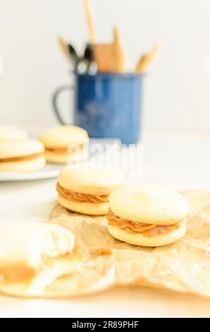 Alfajores Kekse gefüllt mit Dulce de leche. Gestapelt. Küchenutensilien im Hintergrund. Weißer Hintergrund. Stockfoto