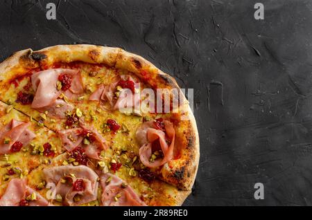 Schinkenpizza in einem Holzofen, schwarzer Hintergrund. Flache Ansicht Stockfoto