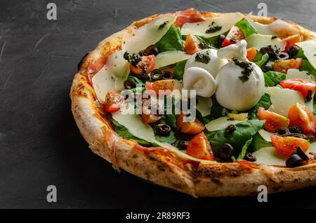 Burrata-Pizza, Kirschtomaten und Pesto-Sauce, zubereitet in einem Holzofen. Schwarzer Hintergrund. Stockfoto