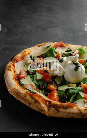 Burrata-Pizza, Kirschtomaten und Pesto-Sauce, zubereitet in einem Holzofen. Schwarzer Hintergrund. Stockfoto