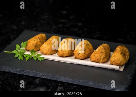 Bolinhos de bacalhau, sehr berühmt in der portugiesischen Gastronomie. Gebratene Teigtaschen, Kabeljauknödel, Fisch, Bacalao bunuelos. Kabeljaukuchen auf dunklem Hintergrund. Stockfoto