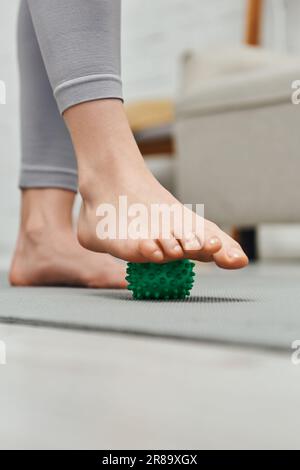 Zugeschnittene Ansicht einer Frau mit Handmassageball bei Fußmassage und Heimstehen auf Fitnessmatte, Körperentspannung und ganzheitlicher Wellness-Praxis Stockfoto