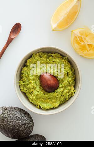 Guacamole mit Knochen in einer weißen Schüssel, weißer Hintergrund, Draufsicht. Gesundes pflanzliches Lebensmittelkonzept. Stockfoto