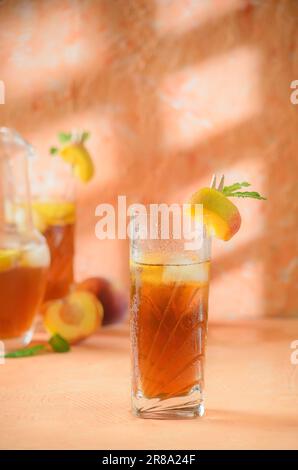 Pfirsich-Eistee-Kanne im Hintergrund. Schatten auf melonenfarbenem Hintergrund. Stockfoto