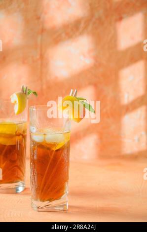 Pfirsich-Eistee-Kanne im Hintergrund. Schatten auf melonenfarbenem Hintergrund. Stockfoto