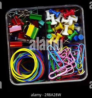 Set aus bunten Schreibwaren, Stecknadeln, Clips, Gummibändern, Klemmen isoliert auf Schwarz. Verschiedene Büromaterialien in einer Plastikbox Stockfoto