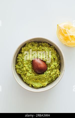 Guacamole mit Knochen in einer weißen Schüssel, weißer Hintergrund, Draufsicht. Gesundes pflanzliches Lebensmittelkonzept. Stockfoto