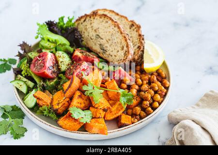 Vegane Mittagspause: Gemüsesalat, gebratene Kichererbsen und gebackene Süßkartoffeln mit gesundem Brot. Gesundes pflanzliches Diätkonzept. Stockfoto