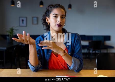 Glückliche, birassistische Geschäftsfrau, die während eines Videoanrufs am Schreibtisch zuhört Stockfoto