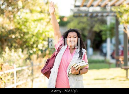 Fröhliche Lateinische Studentenfrau Mit Büchern, Die Im Freien Die Hand Heben Stockfoto