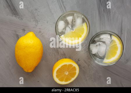 Erfrischendes kaltes Wasser mit Zitrone in Gläsern auf grauem Hintergrund, Draufsicht. Flach liegend, über Kopf, von oben. Stockfoto