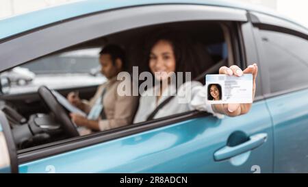 Eine glückliche Frau aus dem Nahen Osten, die im Auto sitzt und den Führerschein vorzeigt Stockfoto