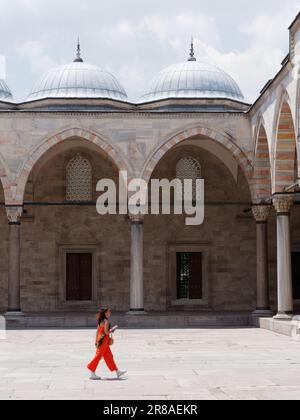 Dame in Orange, die im Innenhof, auch bekannt als Sahn der Suleymaniye-Moschee, Istanbul, Türkei, spaziert Stockfoto