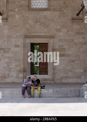 Paare in farbenfroher Kleidung sitzen im Innenhof aka Sahn der Suleymaniye Moschee in Stanbul, Türkei Stockfoto