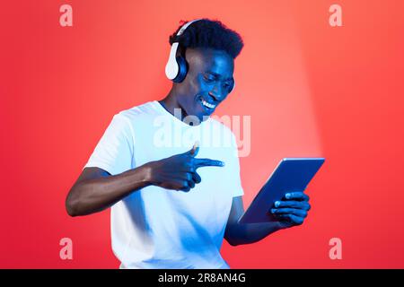 Fröhlicher junger schwarzer Mann mit Headset und digitalem Tablet Stockfoto