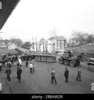 Aktuell 57-3-1960: Riese auf Stadtbesichtigung vierzig Räder, die neulich gemeinsam von Hasle nach Ulven in Oslo gerollt wurden. Sie führten eine historische Aufgabe aus: Der bisher größte in Norwegen gebaute Transformator – ein Riese von 205 Tonnen – wurde von per Kure A/S zum Standort der Beleuchtungsfirma in Ulven transportiert, wo er bei der Stromversorgung helfen wird. Der Transformator, der 161.000 Kilovoltampère erzeugt, ist 9,6 Meter lang und 5,7 Meter breit. Oslo Lysverker hatte Verstärkung für den Großtransport angefordert, und nicht weniger als zwei Fahrer waren im Geschäft. Sie erhielten ihre Fahrbefehle vom Komma Stockfoto