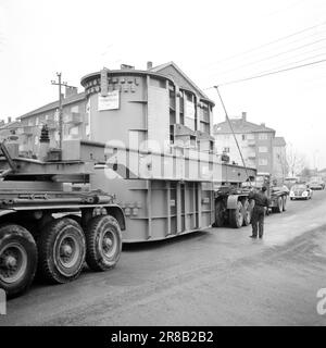 Aktuell 57-3-1960: Riese auf Stadtbesichtigung vierzig Räder, die neulich gemeinsam von Hasle nach Ulven in Oslo gerollt wurden. Sie führten eine historische Aufgabe aus: Der bisher größte in Norwegen gebaute Transformator – ein Riese von 205 Tonnen – wurde von per Kure A/S zum Standort der Beleuchtungsfirma in Ulven transportiert, wo er bei der Stromversorgung helfen wird. Der Transformator, der 161.000 Kilovoltampère erzeugt, ist 9,6 Meter lang und 5,7 Meter breit. Oslo Lysverker hatte Verstärkung für den Großtransport angefordert, und nicht weniger als zwei Fahrer waren im Geschäft. Sie erhielten ihre Fahrbefehle vom Komma Stockfoto