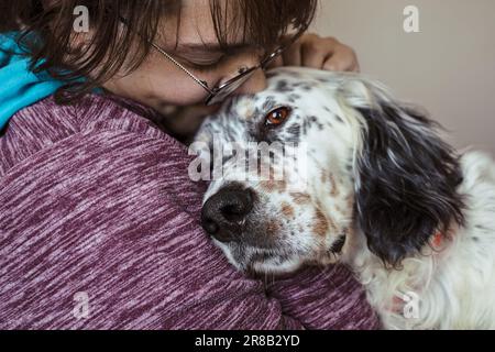 Junge lächelnde Frau umarmt englischen Setter-Hund in einer Hausaufnahme Stockfoto