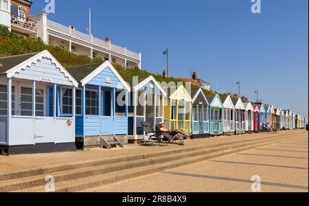 Southwold, Suffolk, Großbritannien. Mann sonnt sich vor den bunten Strandhütten an der Southwold Promenade. Stockfoto