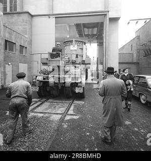 Aktuell 57-3-1960: Riese auf Stadtbesichtigung vierzig Räder, die neulich gemeinsam von Hasle nach Ulven in Oslo gerollt wurden. Sie führten eine historische Aufgabe aus: Der bisher größte in Norwegen gebaute Transformator – ein Riese von 205 Tonnen – wurde von per Kure A/S zum Standort der Beleuchtungsfirma in Ulven transportiert, wo er bei der Stromversorgung helfen wird. Der Transformator, der 161.000 Kilovoltampère erzeugt, ist 9,6 Meter lang und 5,7 Meter breit. Oslo Lysverker hatte Verstärkung für den Großtransport angefordert, und nicht weniger als zwei Fahrer waren im Geschäft. Sie erhielten ihre Fahrbefehle vom Komma Stockfoto