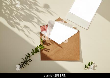 Beigefarbener Papierumschlag mit Fotografiemodell, grüner Zweig unter Schatten. Sammlung von Grußkarten, Postkarten, Einladungen Stockfoto