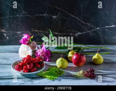 Stille Früchte: Birnen, Apfel, Teller mit Erdbeeren, Salatblätter und frische Pfingstrosen auf dunklem Marmorhintergrund, Platz für Text Stockfoto
