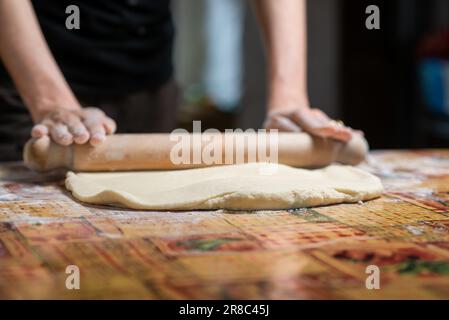 Eine Frau rollt Teig mit einem Rollnadel aus. Zubereitung von Teig für Teigtaschen, Teigtaschen, Kuchen. Stockfoto