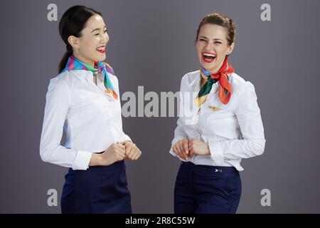 Lächelnde, stilvolle Stewardess in blauem Rock, weißem Hemd und Schal vor grauem Hintergrund. Stockfoto