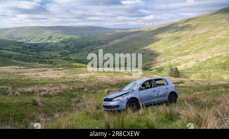 Ein Auto wurde auf einer steilen Bergweide zerstört, nachdem er von einer engen Landstraße in Dentdale, Cumbria, Großbritannien, abgekommen war. Stockfoto