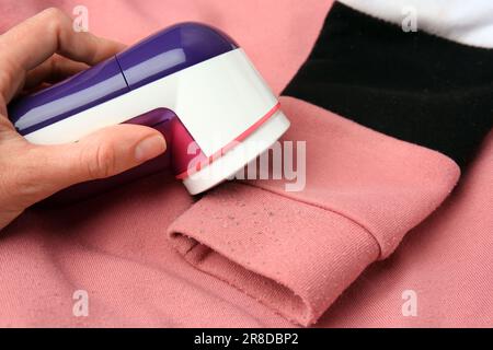 Frau, die einen modernen Stoffrasierer auf einem Pullover mit Fusseln und Nahaufnahme benutzt Stockfoto
