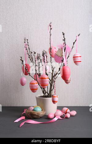 Wunderschöne Weidenzweige mit bemalten Eiern und Ostern-Dekor auf hellgrauem Holztisch Stockfoto