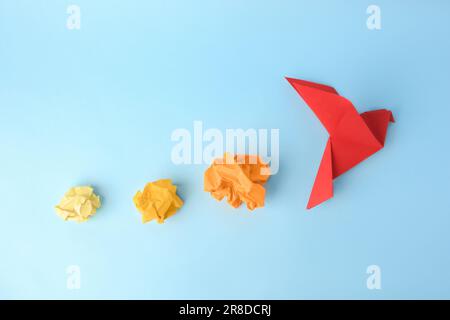 Handgefertigter roter Vogel und zerknitterte Papierstücke auf hellblauem Hintergrund, flach liegend Stockfoto