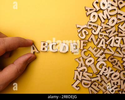 Die Hand einer Person ordnet Holzbriefe in der Reihenfolge von ABCDE auf gelbem Hintergrund an Stockfoto